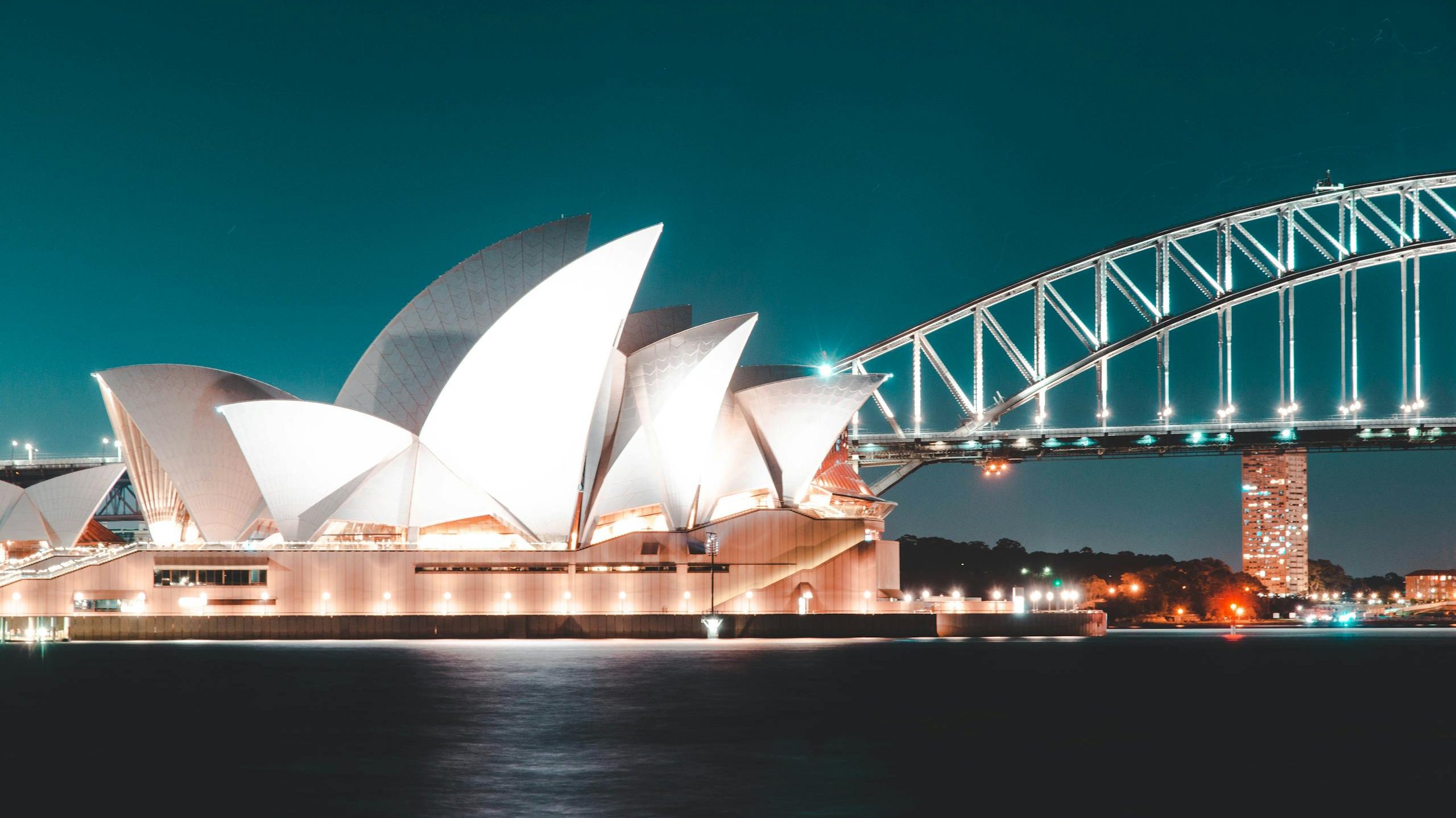 Stunning night view of Sydney Opera House and Harbour Bridge, beautifully illuminated against a clear sky.